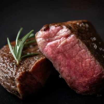 A close up image of two thick beef steaks, cooked with pink insides and some rosemary on a plate.